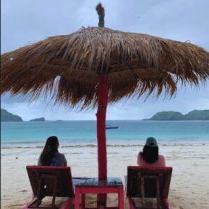 Adults Only Kuta Lombok beach view with two guests relaxing under a thatched umbrella on a quiet tropical beach