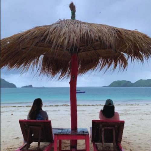 Adults Only Kuta Lombok beach view with two guests relaxing under a thatched umbrella on a quiet tropical beach