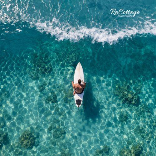 Aerial view of surfer sitting on board waiting for waves during Kuta Lombok Surf session over clear reef water