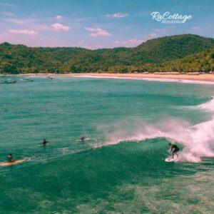 Kuta Lombok Surf scene with surfers riding clear turquoise waves near tropical beach and green hills