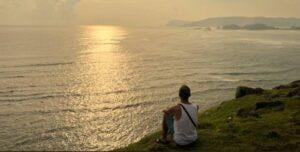 Traveler sitting on Merese Hill overlooking the golden sunset and calm sea in Lombok.