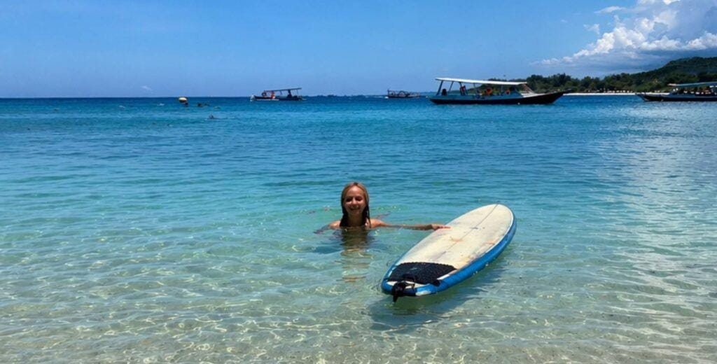 Woman swimming in clear turquoise water at Gerupuk Bay Lombok with boats and gentle waves in the background