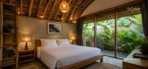 Where to stay in Kuta Lombok cozy tropical bedroom villa with curved bamboo ceiling, wooden bed, warm lighting, and lush garden view near Kuta Center