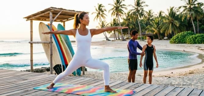 Woman practicing surf and yoga retreat warrior pose on beach deck with colorful surfboards at sunset