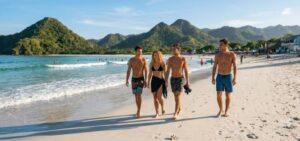 Selong Belanak beach group of travelers walking along white sand shoreline with surfers in water and iconic green pyramid hills in background